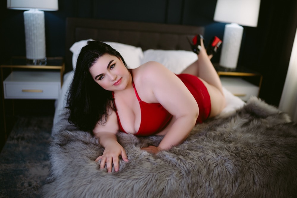 curvy brunette laying on bed with red lingerie in boudoir studio